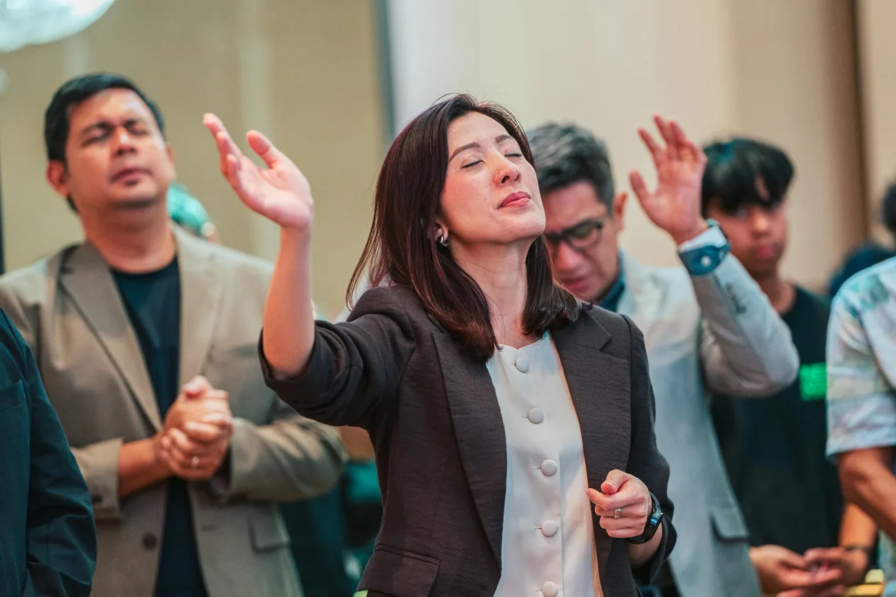A woman lifting her hand in praise during Sunday worship, the congregation singing around her